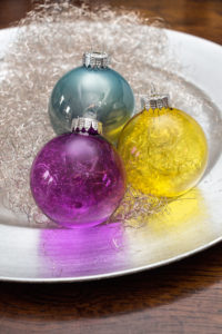 Transparente Weihnachtskugeln in den leuchtenden Farben Lila, Gelb und Petrol.
